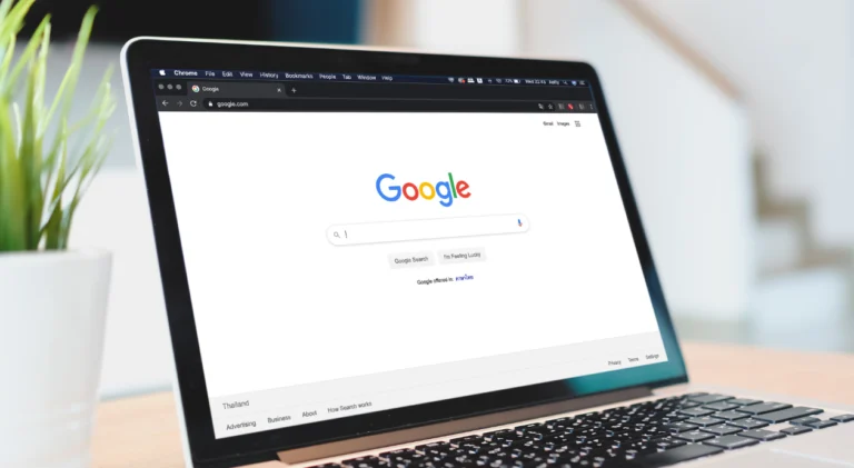 Tela de um laptop exibindo a página inicial de busca do Google aberta no navegador Chrome sobre uma mesa de madeira.