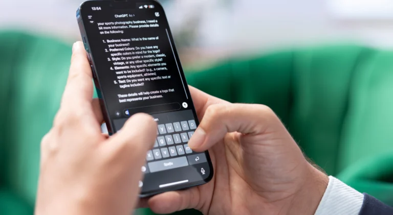 Mãos de uma pessoa branca segurando um smartphone com a tela do ChatGPT aberta, exibindo uma conversa com perguntas geradas pela IA sobre um negócio de fotografia esportiva.