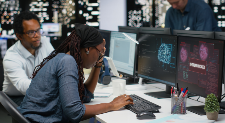 Mulher profissional de tecnologia com expressão preocupada diante de monitores exibindo alertas de sistema hackeado e visualizações de rede, em um ambiente de centro de operações de segurança.