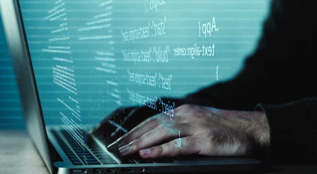 Mãos digitando em notebook com linhas de código projetadas sobre a tela em tons de azul esverdeado.