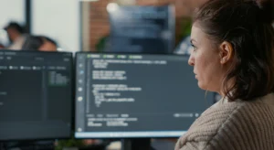 Mulher analisando código em dois monitores, representando a configuração técnica de Open Graph em uma página web.