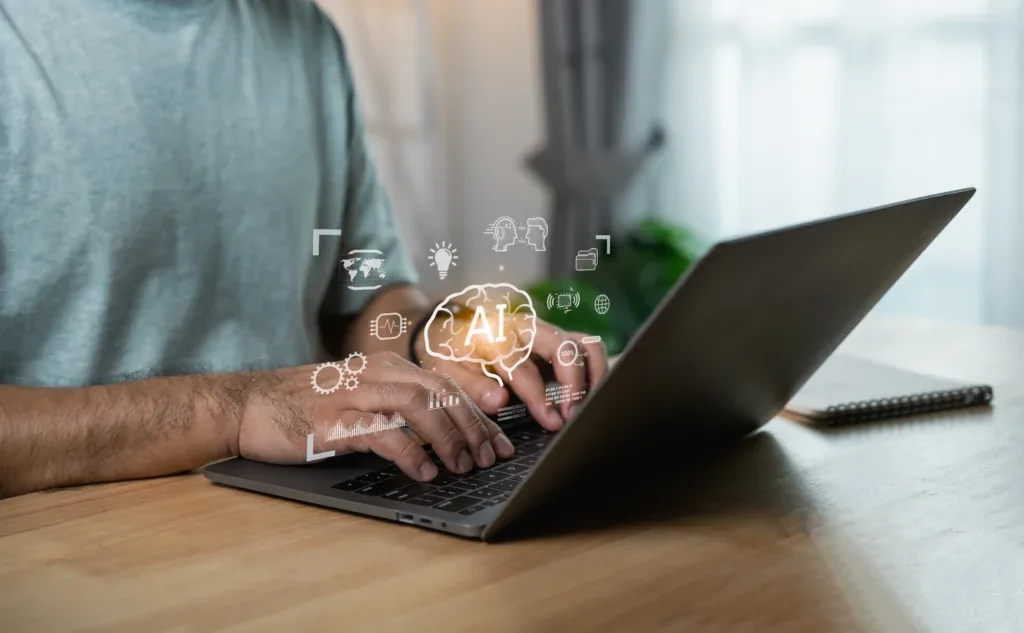 Mãos digitando em um notebook sobre uma mesa de madeira, com ícones de Inteligência Artificial sobrepostos à imagem, incluindo um cérebro com a sigla "AI", engrenagens, gráficos e símbolos de conectividade global.