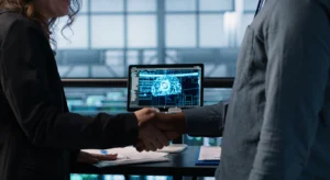 Duas pessoas apertando as mãos em ambiente corporativo, com um monitor ao fundo exibindo a ilustração de um cérebro digital, representando uma parceria em torno de inteligência artificial.